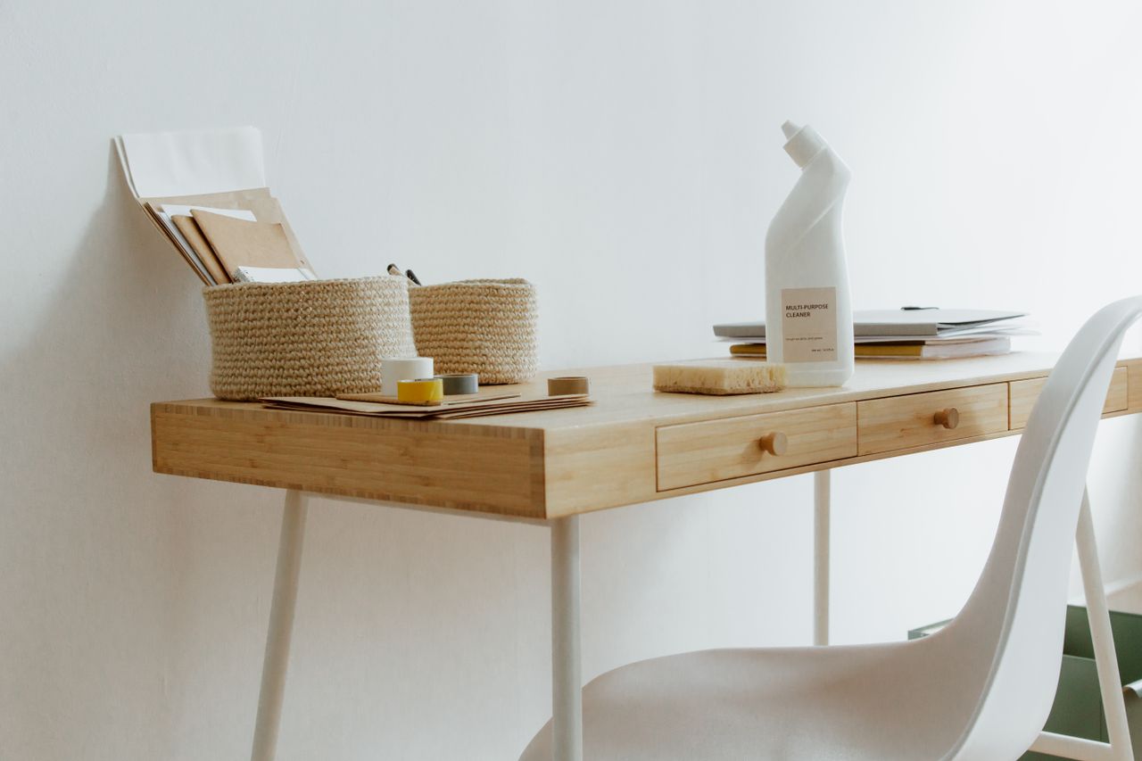A neat, orderly home office desk with cleaning supplies, papers, and storage baskets.